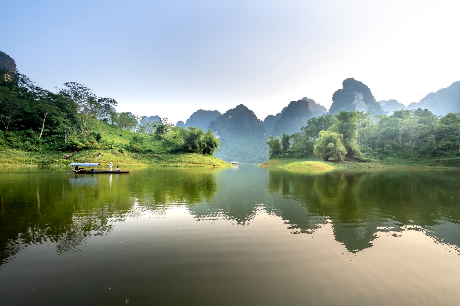 Scenic landscape of of boat floating on peaceful lake with clear water reflecting lush green trees and rocky mountains a