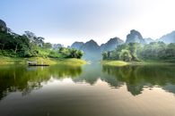 Scenic landscape of of boat floating on peaceful lake with clear water reflecting lush green trees and rocky mountains against cloudless blue sky