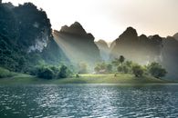 Massive limestone mountains covered with lush green tropical trees near picturesque lake with rippling water under cloudless sunset sky in Tuyen Quang province of Vietnam