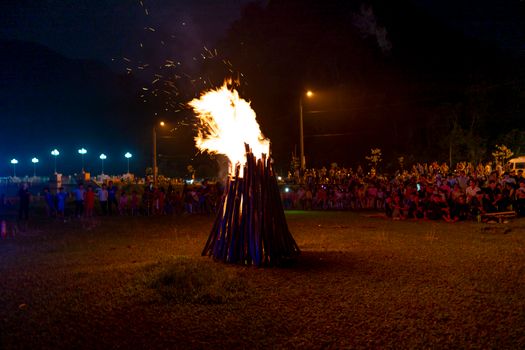 Big burning fire on grassy lawn near crowd of unrecognizable people during traditional festival of Pa Then people in Vietnam