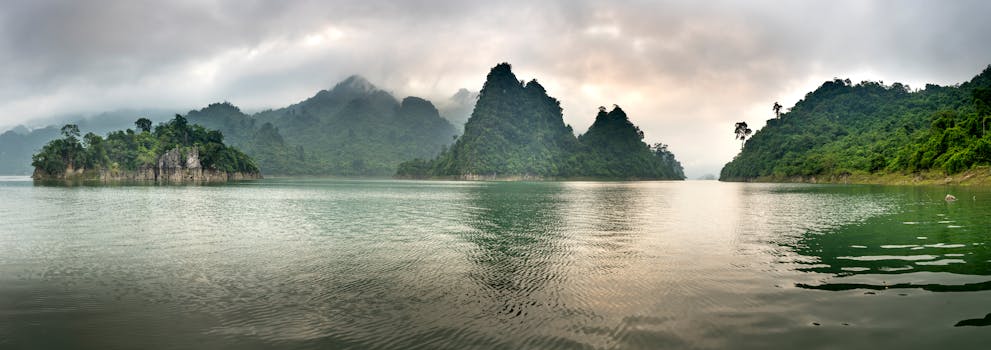Wide angle scenery of pond surrounded by hills covered with lush tropical forest under gray clouds