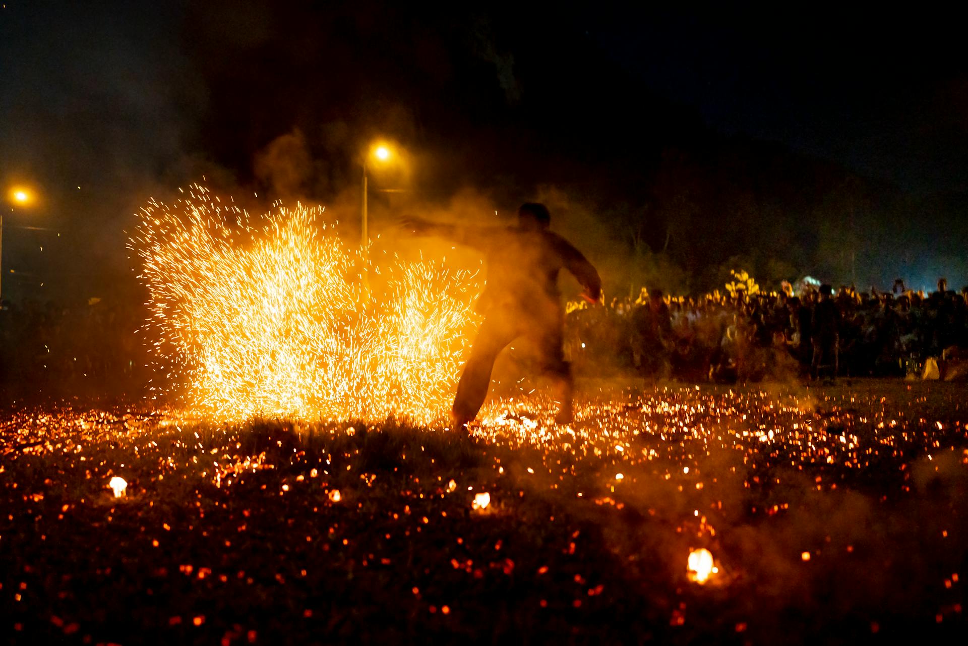 Full body silhouette of unrecognizable male doing performance in bright sparks of fire in dark night