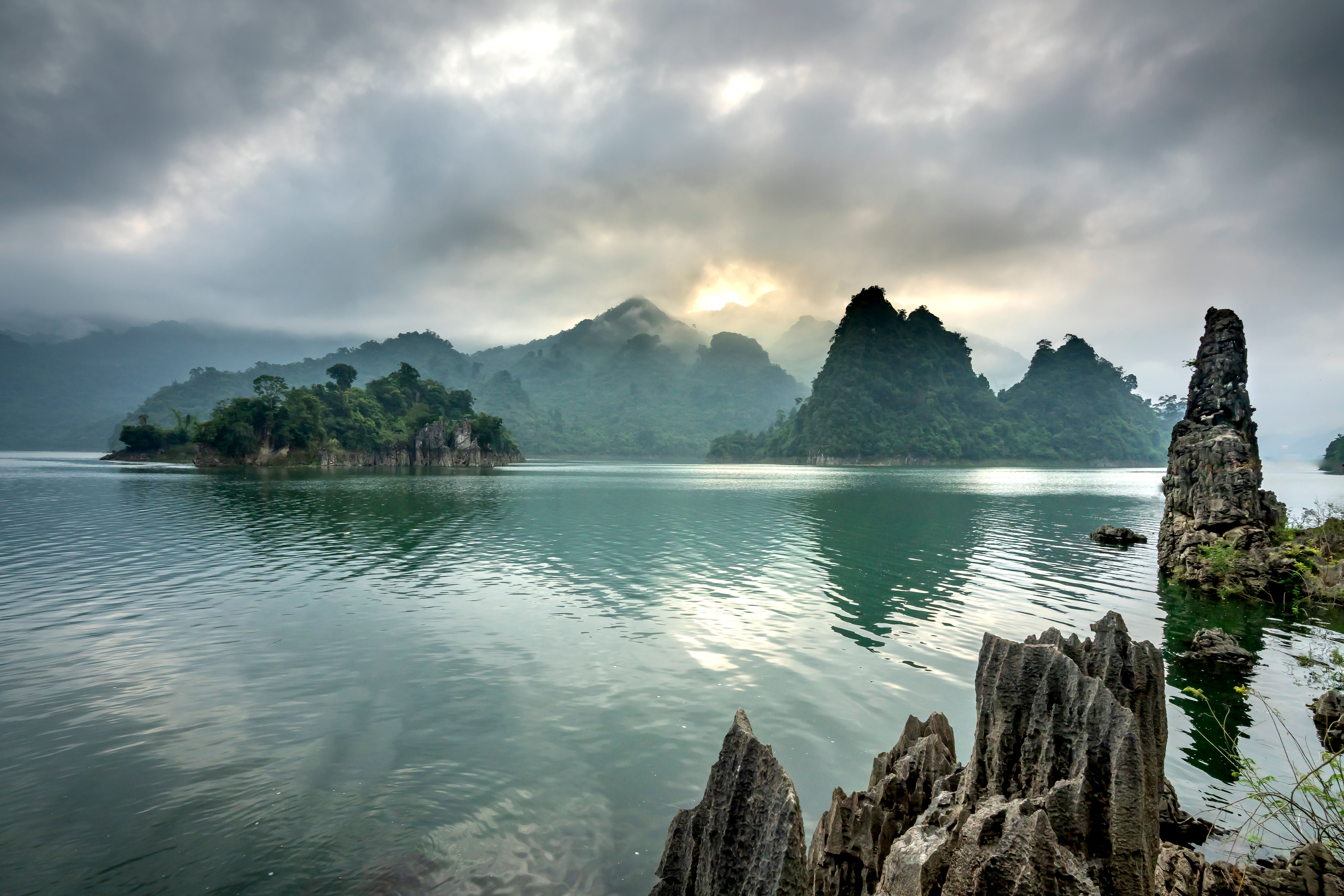 Scenery of rippling pond with clean rippling water surrounded by hills covered with woods under cloudy sky