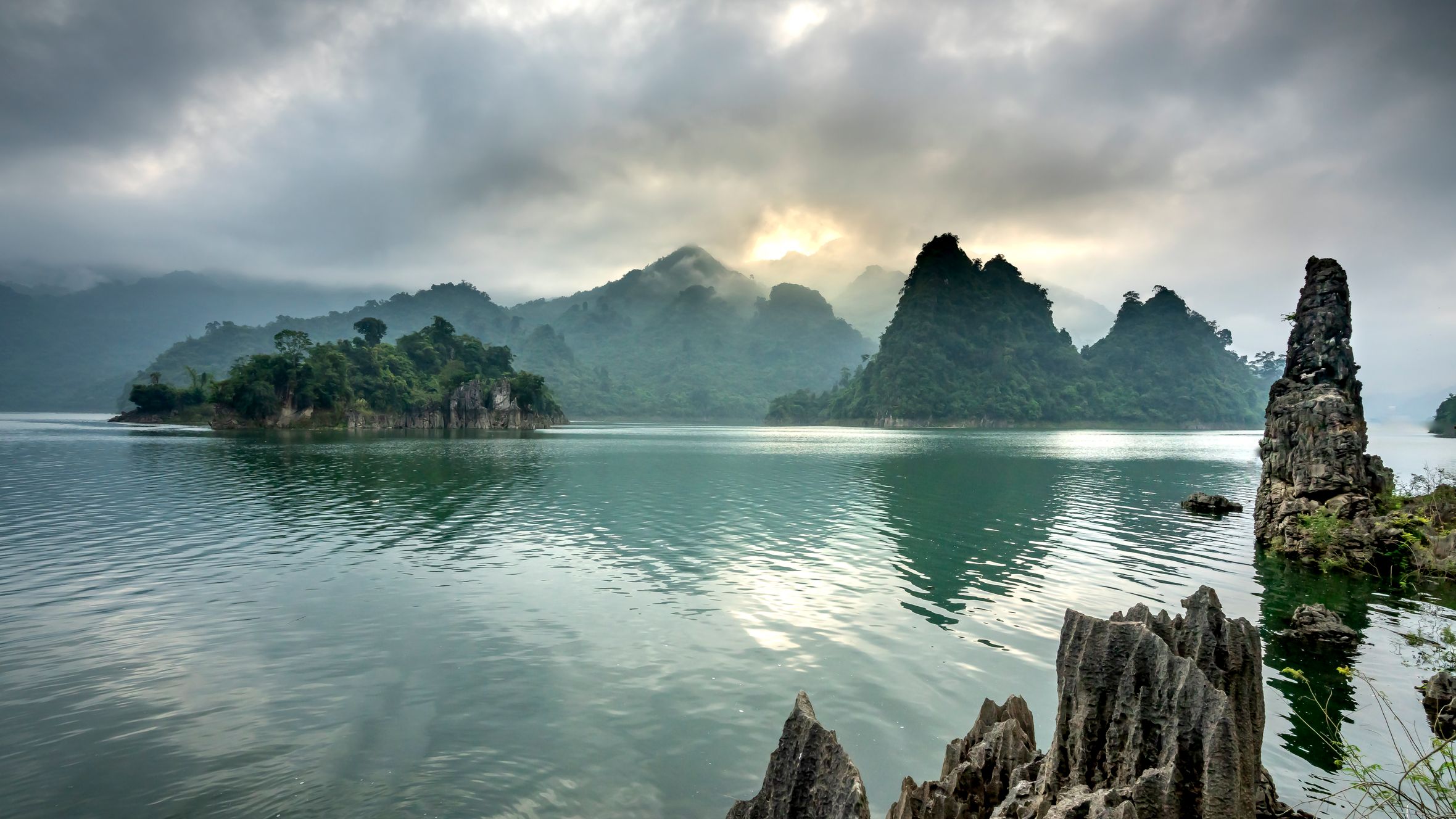 Scenery of rippling pond with clean rippling water surrounded by hills covered with woods under cloudy sky
