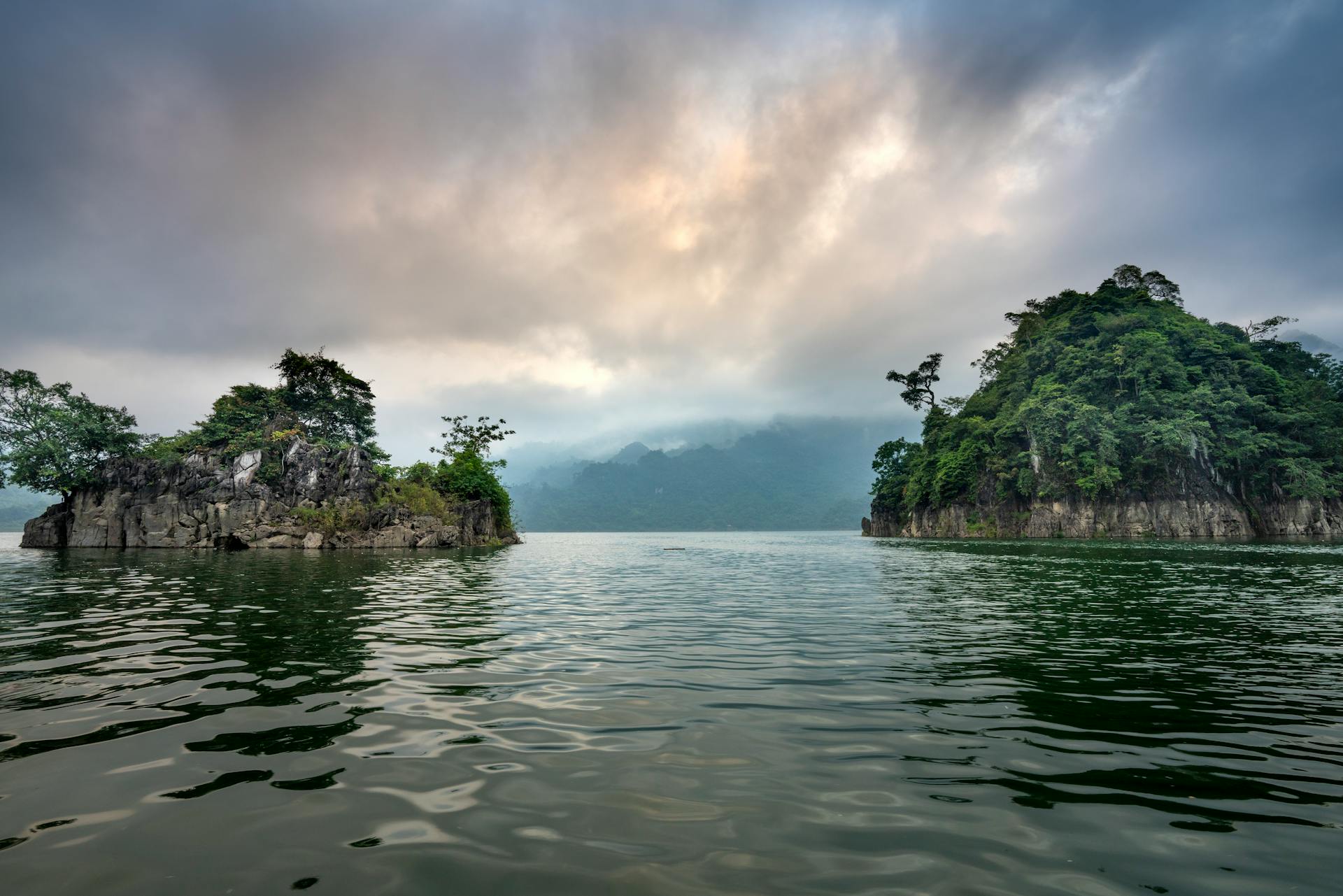 Scenery of lake flowing among rocky formations covered with abundant green plants under clouds