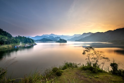 Spectacular view of majestic mount silhouettes against river and trees under colorful sky at sunset in misty weather