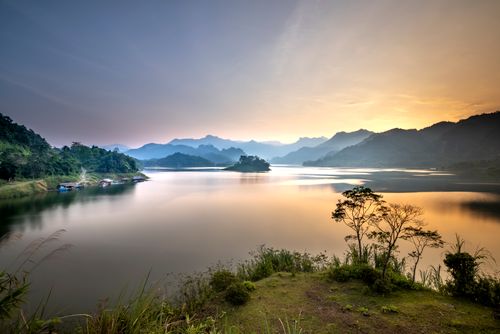 Free Spectacular view of majestic mount silhouettes against river and trees under colorful sky at sunset in misty weather Stock Photo