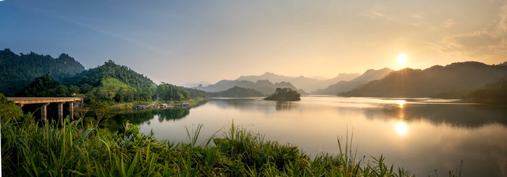 Captivating sunset over a tranquil lake surrounded by lush green mountains and a serene landscape.