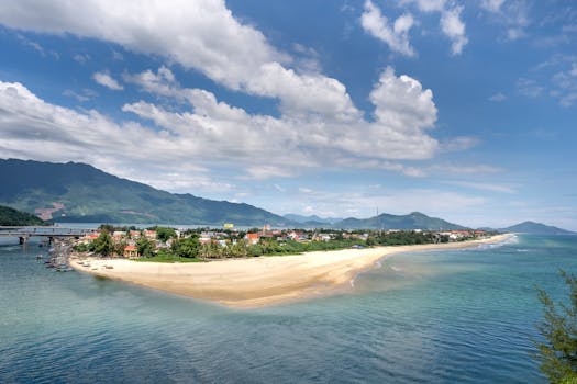 Picturesque coastal village with a sandy beach and mountain views under a bright blue sky.