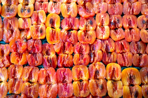 From above of pile of fresh ripe juicy halved persimmons placed on stall and sun drying