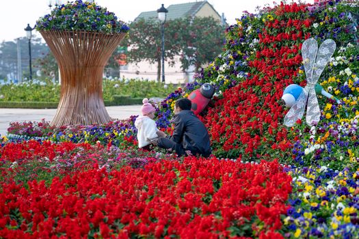 Anonymous dad interacting with toddler girl among blossoming pansies and Salvia flowers with decorative dragonfly in park