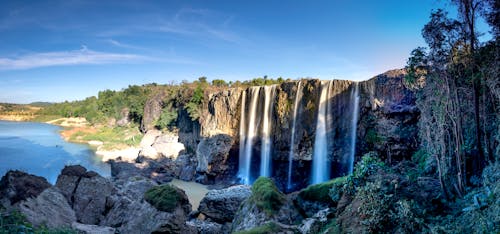 Waterfalls on mountain against river under blue sky