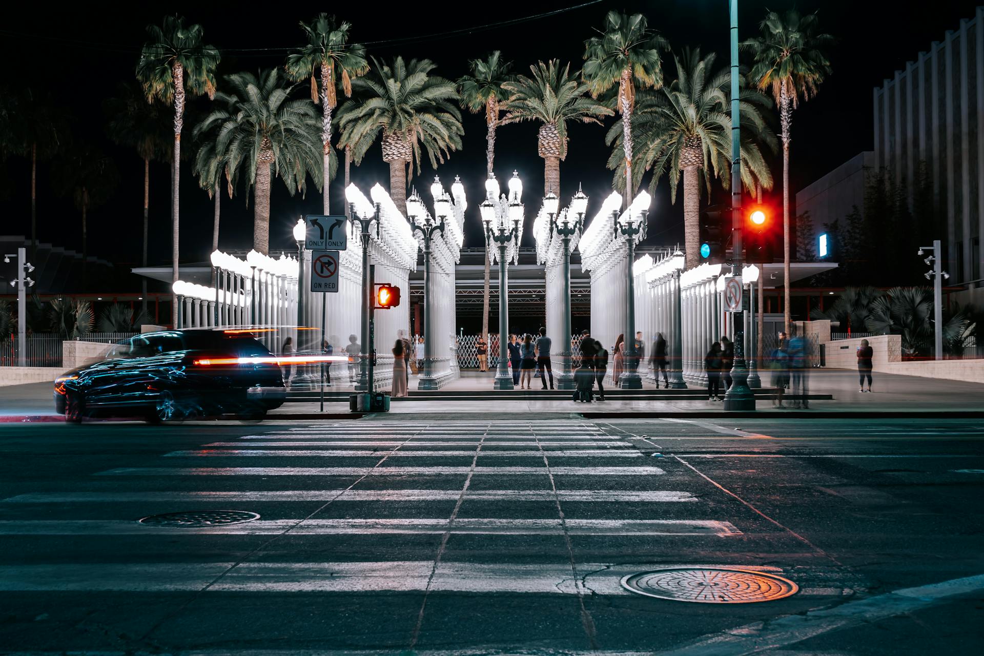 Lively night scene of Urban Light installation with palm trees and pedestrians in LA.