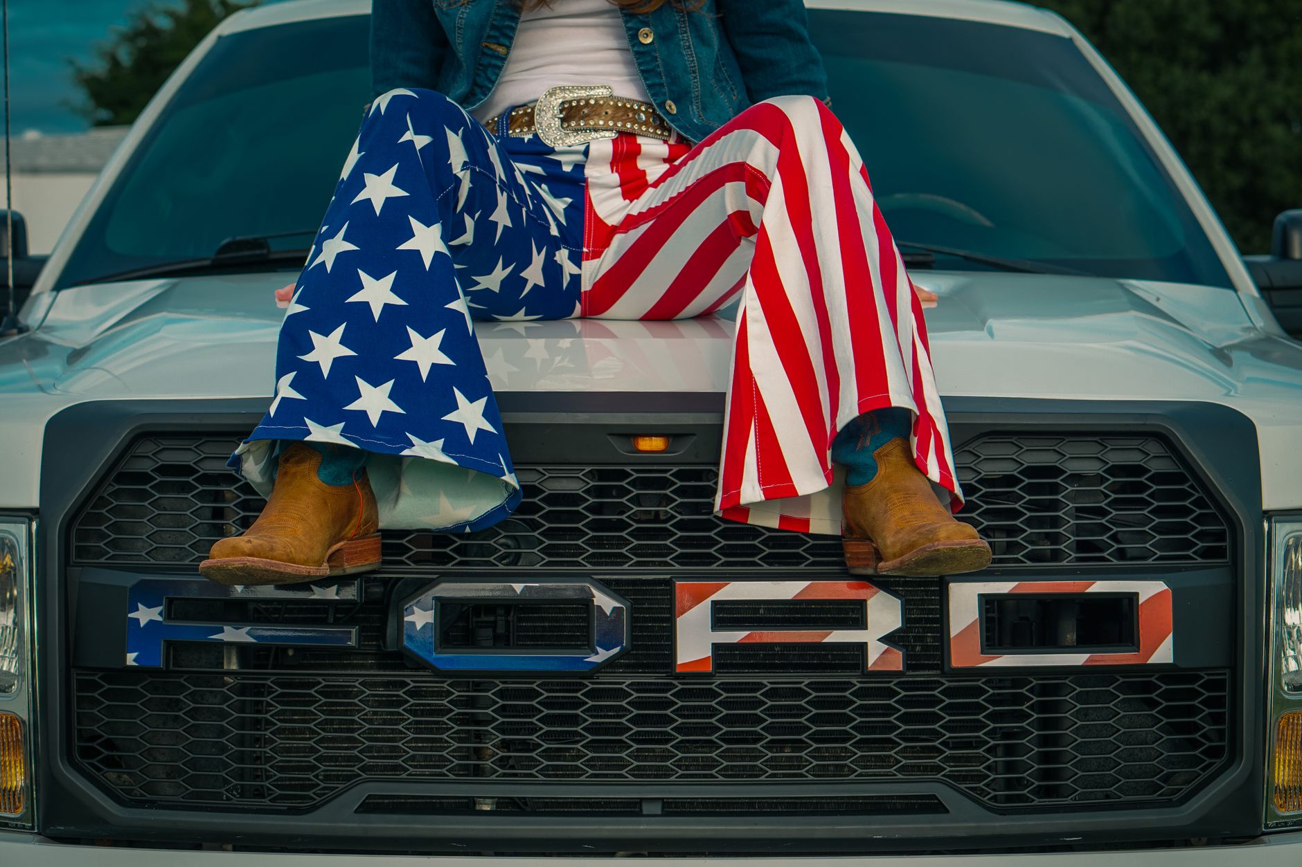 A person in USA flag pants sits on a Ford truck, symbolizing American pride.