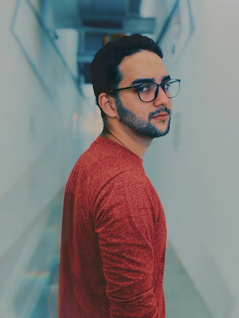 Portrait of a man with glasses and beard, wearing a red sweater, in a corridor.