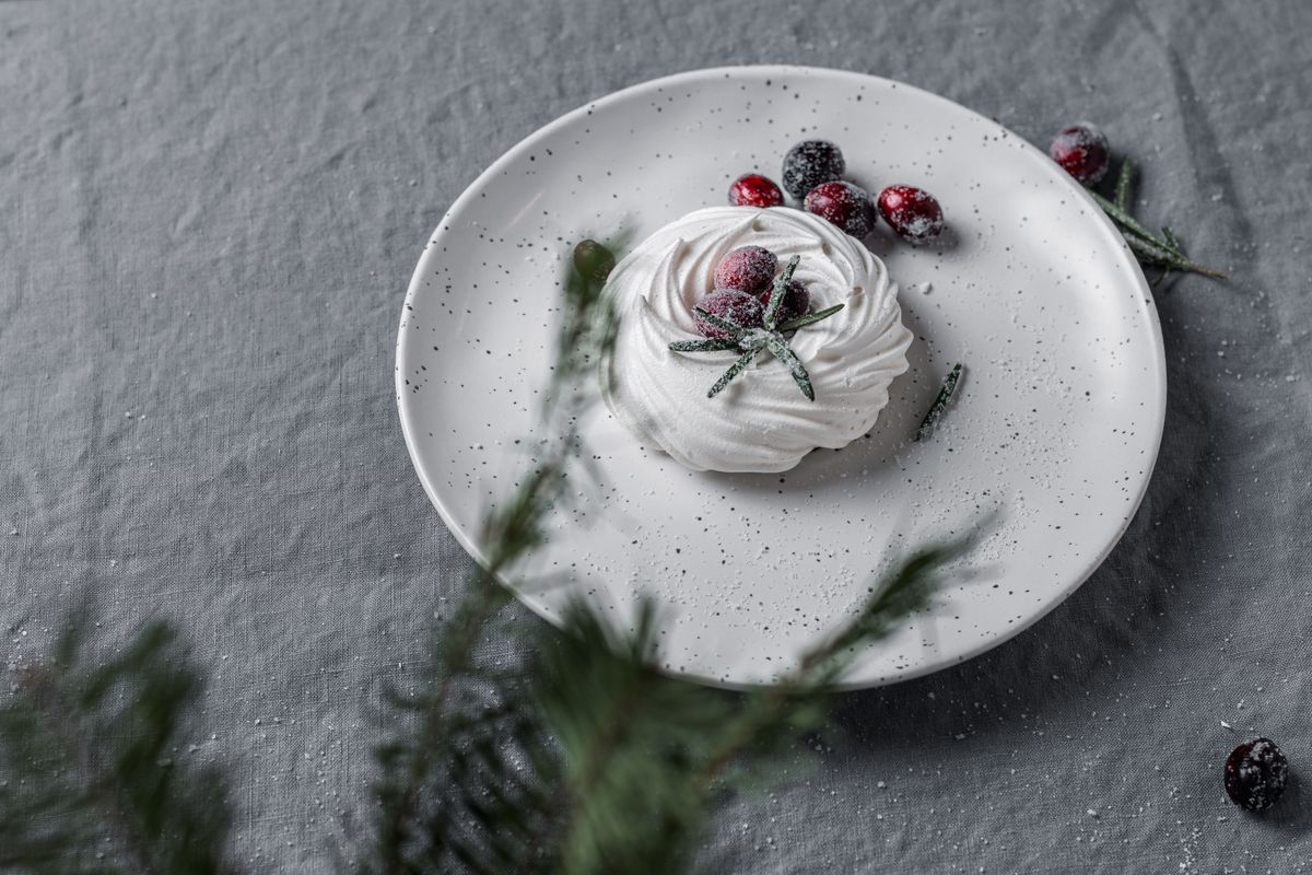 Artistic presentation of a meringue with sugared cranberries and rosemary, perfect for winter.