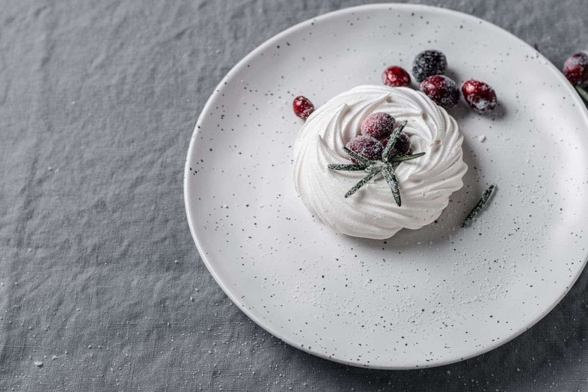 A delicious meringue dessert topped with sugared cranberries on a speckled plate, showcasing food artistry.