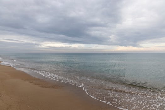 Serene seascape with gentle waves on a sandy beach under a cloudy sky.