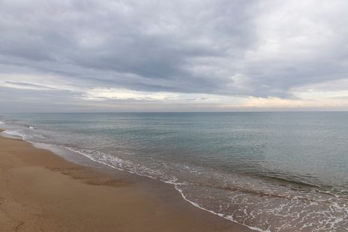 Free Serene seascape with gentle waves on a sandy beach under a cloudy sky. Stock Photo