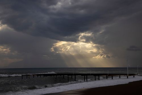 Free Captivating view of sun rays through clouds over sea with wooden dock in foreground. Stock Photo