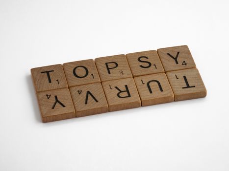 Close-up of wooden Scrabble tiles arranged to spell 'topsy turvy' on a white background.