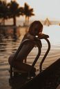 Woman in Black Tank Top Sitting on Chair by the Lake during Sunset