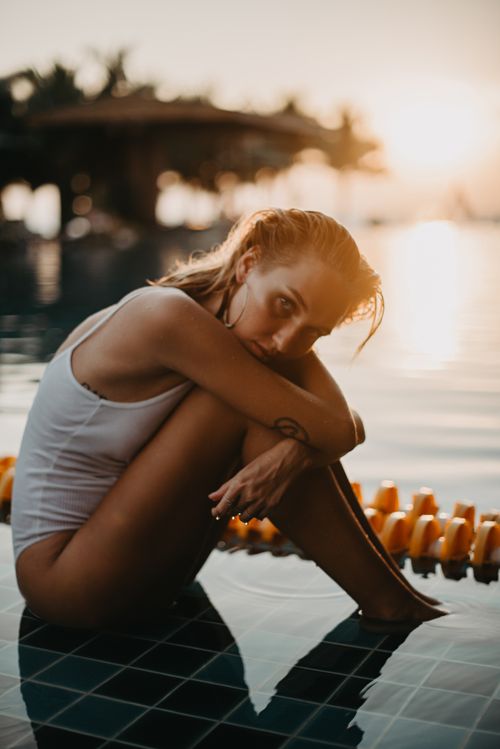 Free A woman in swimwear relaxes poolside in Bali, Indonesia during a serene sunset. Stock Photo