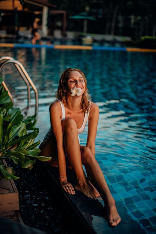 Free Young woman in swimwear enjoying a sunny day poolside with vibrant tropical vibes. Stock Photo