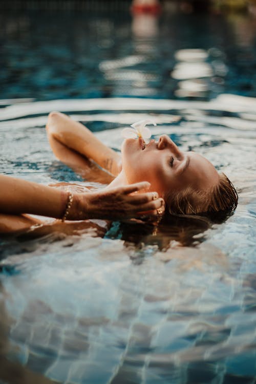 Photo of a Woman in a Swimming Pool with a Flower on Her Mouth