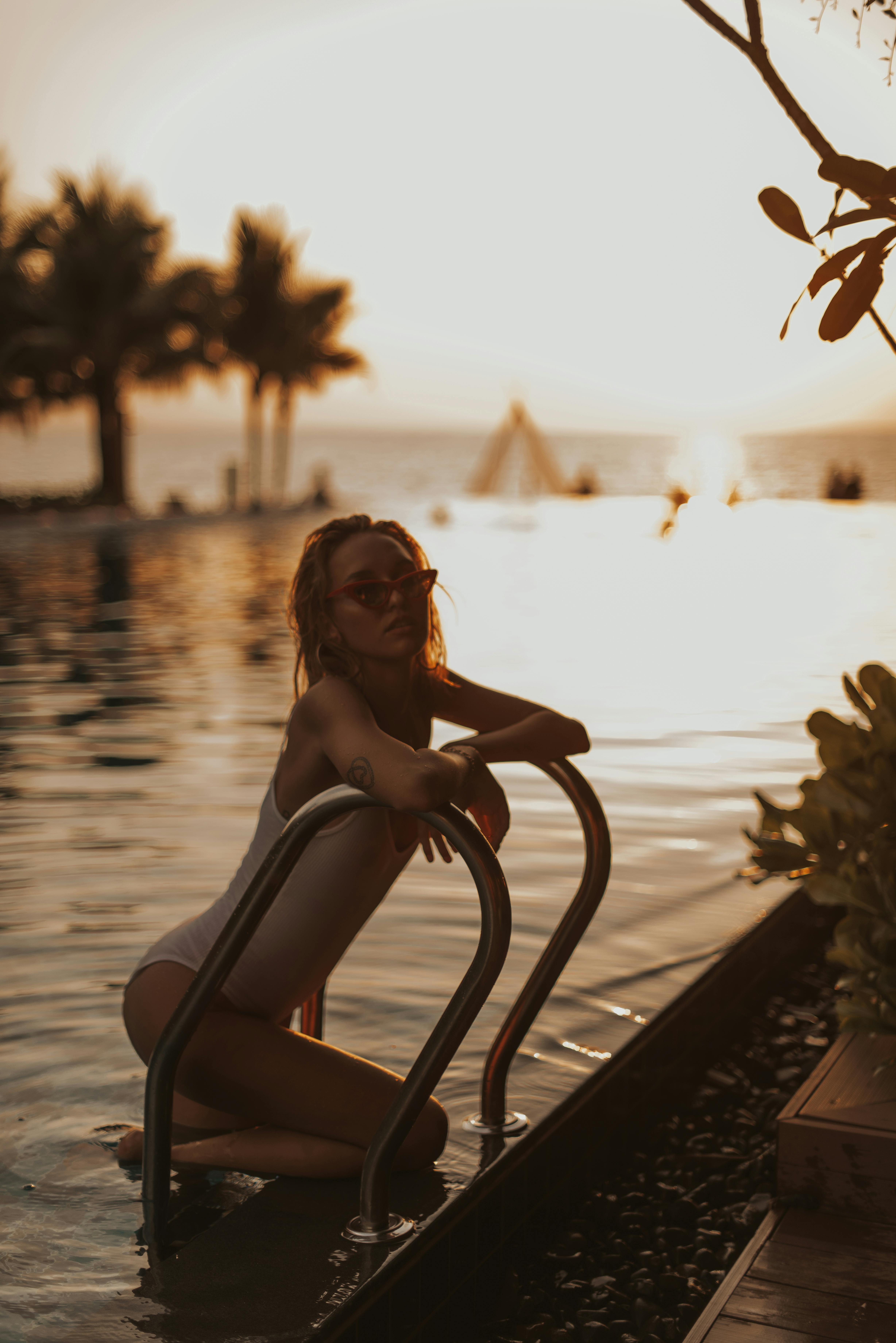 woman in white tank top sitting on brown wooden bench during sunset