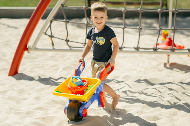 A little boy playing in the sand with a wheelbarrow