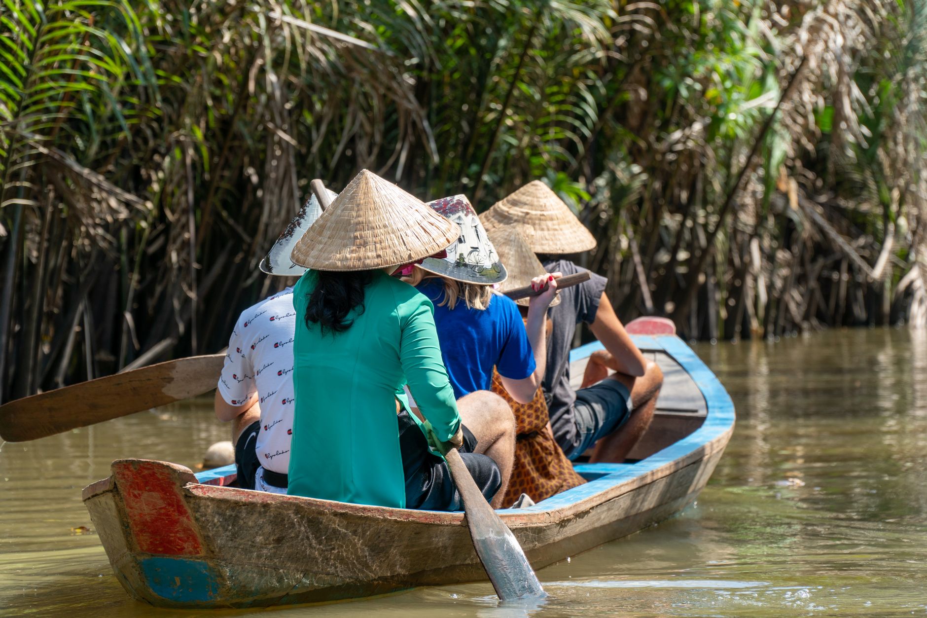 Experience traditional Vietnamese paddling through lush rivers with locals wearing iconic conical hats.