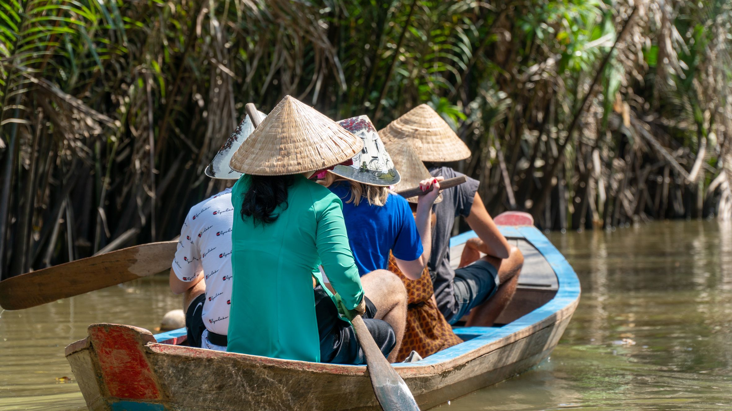 Experience traditional Vietnamese paddling through lush rivers with locals wearing iconic conical hats.