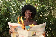Trendy black woman reading burning newspaper in garden