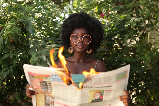 Trendy black woman reading burning newspaper in garden
