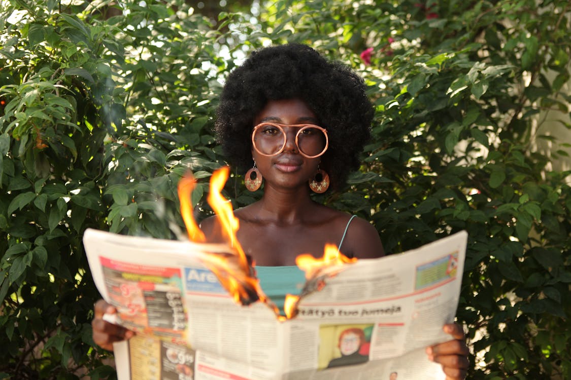 Free Trendy black woman reading burning newspaper in garden Stock Photo