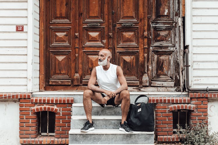 Senior Ethnic Man In Shorts Sitting On Doorsteps