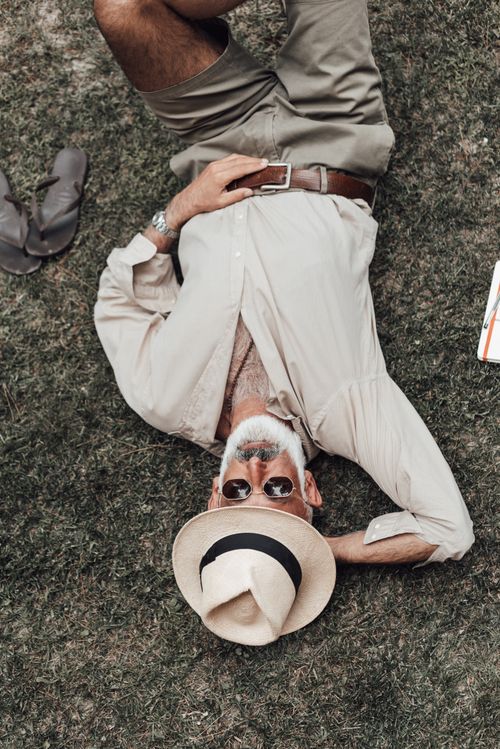 Free From above senior ethnic male wearing trendy summer clothes lying on lush grass with hand behind head and enjoying warm weather Stock Photo