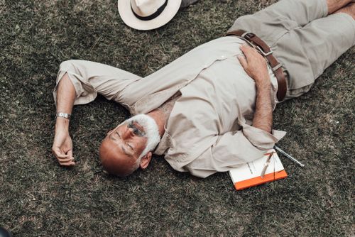 Free High angle relaxed senior male in trendy summer wear lying with eyes closed on verdant grass and enjoying warm day Stock Photo