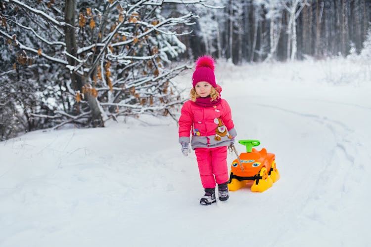 Girl In Pink Jacket Dragging A Toy While Walking On Snow