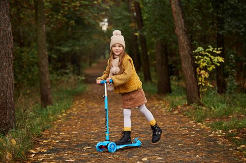Free Happy child in winter clothes riding a scooter along a forest path in autumn. Stock Photo
