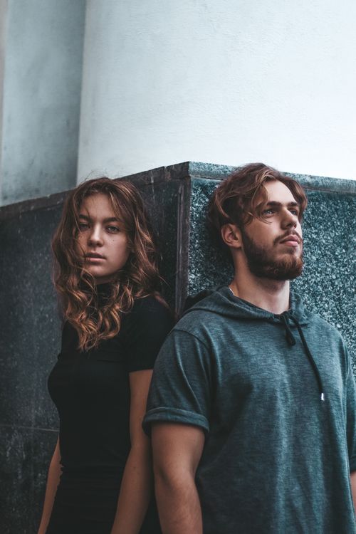 Free Young man and woman leaning against a marble wall, capturing a modern and relaxed urban style. Stock Photo