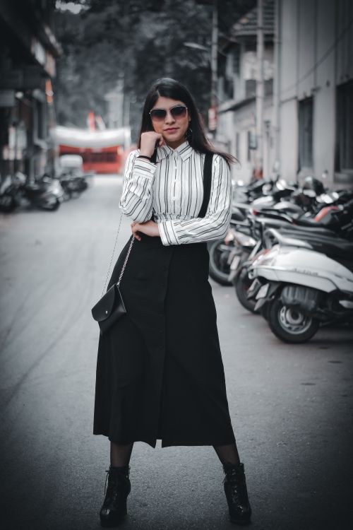 Free Stylish young woman in black skirt and sunglasses standing confidently on a city street. Stock Photo