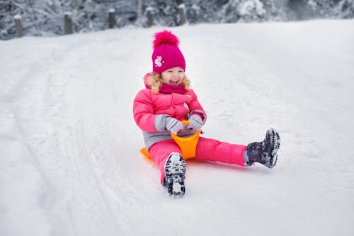 Kid Wearing Pink Winter Clothes Riding on a Sled on Snow Covered Ground