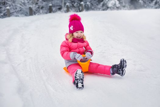 A joyful child sledding on snow-covered ground, dressed in vibrant winter clothes.