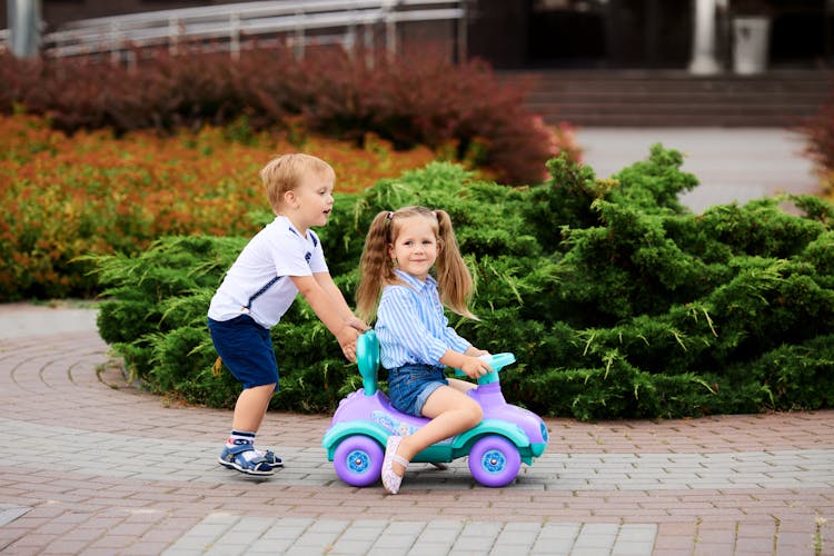 Boy Pushing A Girl Riding In Toy Car