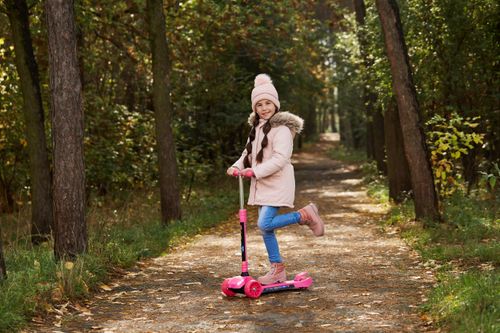 Free Smiling girl with beanie riding a scooter on a tree-lined path in autumn. Stock Photo