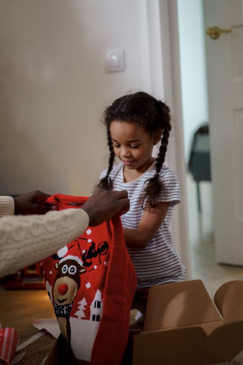 Free A father and daughter joyfully unbox a Christmas sweater together indoors. Stock Photo