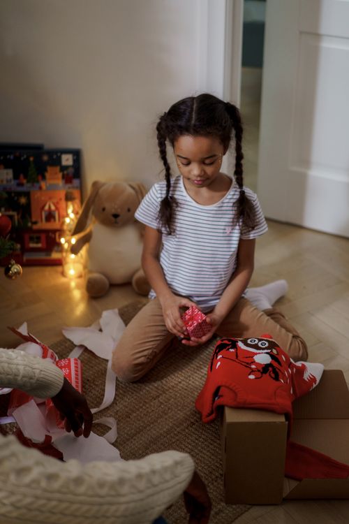 Free A young girl joyfully unboxes a Christmas present indoors, surrounded by holiday decor. Stock Photo