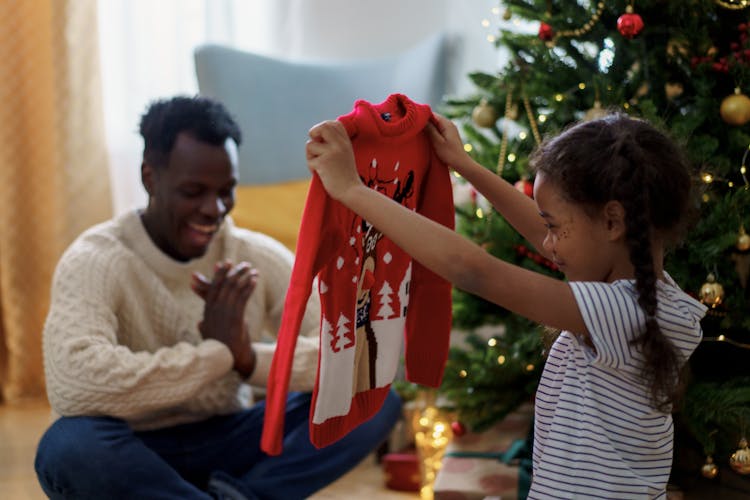 A Girl Smiling While Holding A Red Christmas Sweater